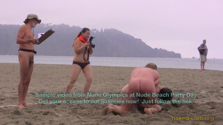 2. Two naked guys are “Wrestling clothing-free at a beach festival”. Also, topless photographer’s boobs are visible in the background